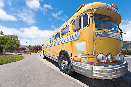 An old classic yellow shcool bus is parked next to curb.