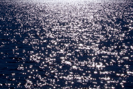 A mass of sunlight sparkles on a calm sea in black and white