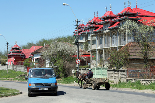 Hateg, Hunedoara, Romania - April 23, 2015:  Gypsy people driving a van and a cart on the street in front of a big Rom house in the suburb of a Romanian town.