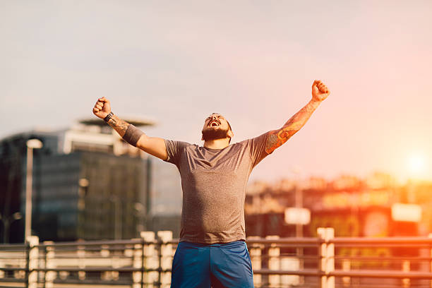 I Did It! Male Runner Jogging in the city and finishing his training with his hands up in the air screaming with happiness. He made his goal! center athlete stock pictures, royalty-free photos & images