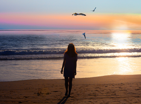 young woman walking on the beach at sunset