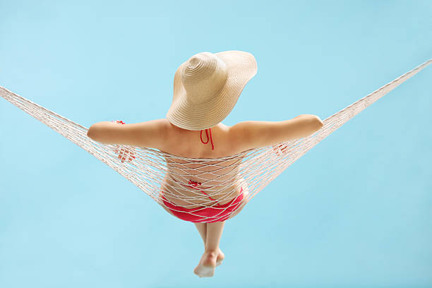 Rear view studio shot of a young girl with a stylish hat lying in a hammock on blue background