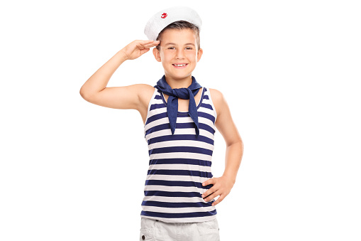Joyful little boy in a sailor uniform saluting towards the camera and smiling isolated on white background