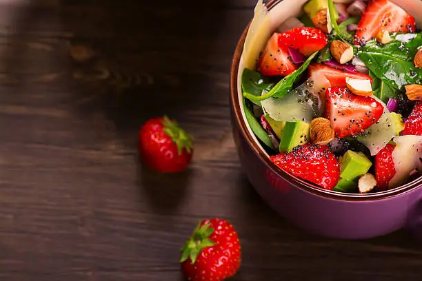 Fresh summer salad with strawberry,avocado and spinach on rustic wooden background. Selective focus