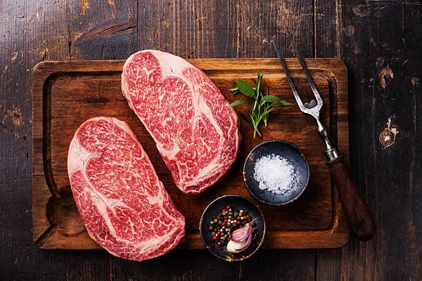 Two Raw fresh marbled meat Black Angus Steak Ribeye, seasonings and meat fork on dark wooden background