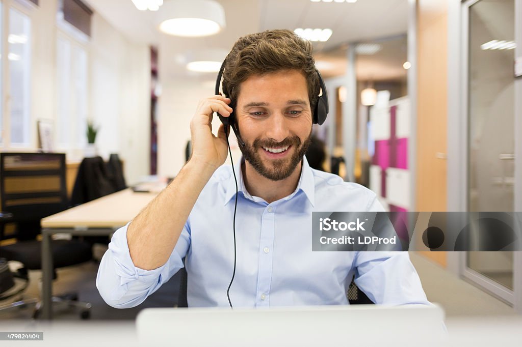 Smiling Businessman in the office on video conference, headset, Close up of a hipster man in conference call at his desk  facing camera IT Support Stock Photo