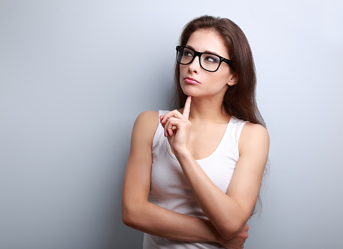 Beautiful serious thinking young woman looking up on empty copy space