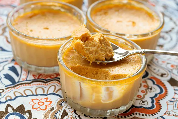 Homemade pumpkin creme brulee in glass bowls with patterned tablecloth background.