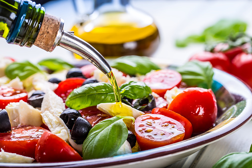 Caprese. Caprese salad. Italian salad. Mediterranean salad. Italian cuisine. Mediterranean cuisine. Tomato mozzarella basil leaves black olives and olive oil on wooden table. Recipe - Ingredients