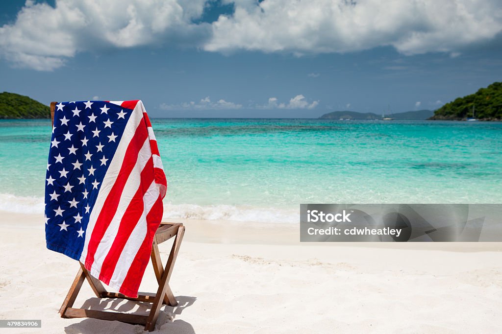 American flag towel over beach chair in US Virgin Islands single teak chair and a towel with American flag on it at a beach in US Virgin Islands Beach Stock Photo