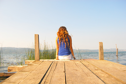 Young woman sitting on a jetty near a beautiful lake in summer.