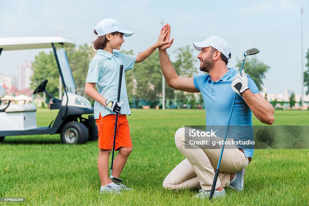 My little winner! Cheerful young man and his son giving high-five to each other while standing on the golf course Golf Stock Photo