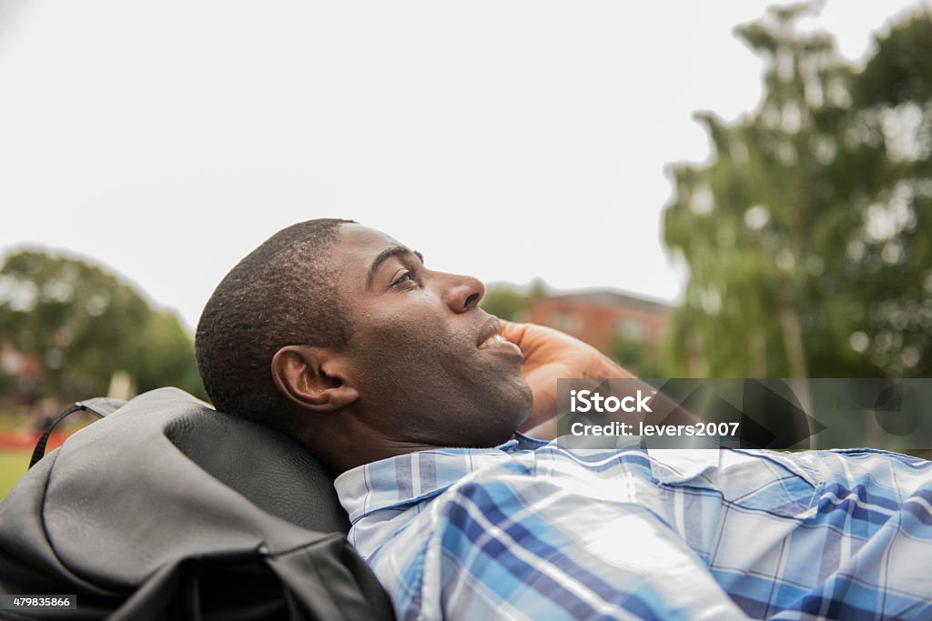 Handsome man on phone in park Young man lying in park against his bag on phone  2015 Stock Photo