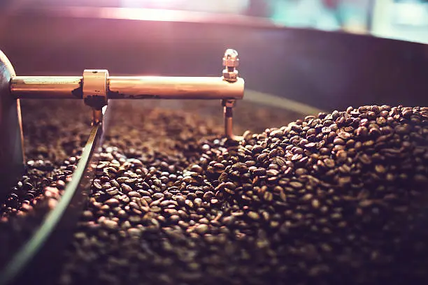 The process of roasting a batch of high quality single origin coffee beans in a large industrial roaster; the toasted beans are in the cooling cycle.  Horizontal image with copy space.  High contrast with colorful tones.