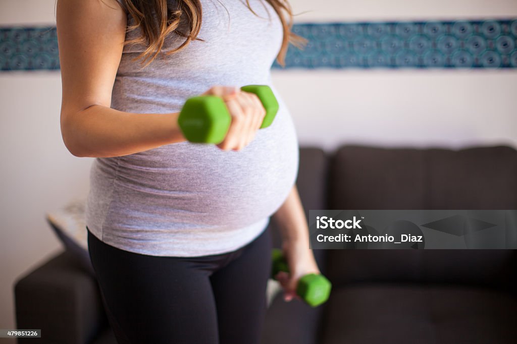 Pregnant woman lifting weights Closeup of a pregnant brunette exercising at home with a couple of dumbbells 20-29 Years Stock Photo