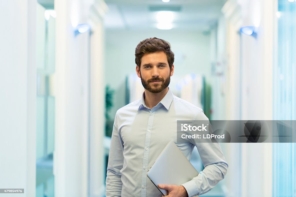 Portrait of handsome bearded business man in corridor office Business man hipster style with laptop in office. looking at camera Men Stock Photo