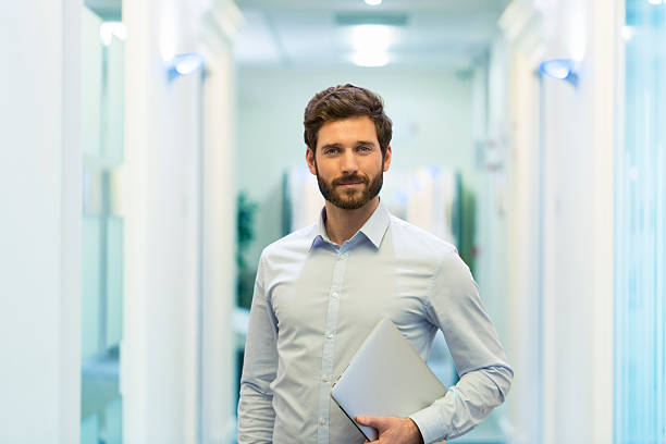 Portrait of handsome bearded business man in corridor office Business man hipster style with laptop in office. looking at camera man 30 years old stock pictures, royalty-free photos & images
