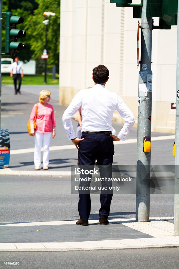 Waiting caucasian businessman at traffic light and crosswalk Frankfurt Main, Germany - July 3, 2015: Rearshot of a waiting caucasian adult businessman standing at traffic light and crosswalk of street Taunusanlage in Frankfurt Main in summer. In background a woman is waiting on opposite side of street. 2015 Stock Photo