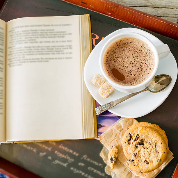 Hot chocolate in white cup, cookies, book, blanket, rustic wood background