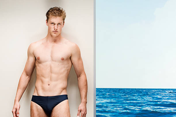 a petto nudo muscolare uomo appoggiato da muro in spiaggia - men swimming trunks beach racing briefs foto e immagini stock