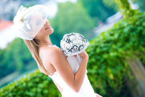 Bride holding wedding bouquet at wedding ceremony. She is happy with smile on her face. Green background. Copy space.