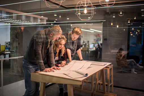 Group of creative people having a meeting in the office and working on blueprints. The view is through the glass.