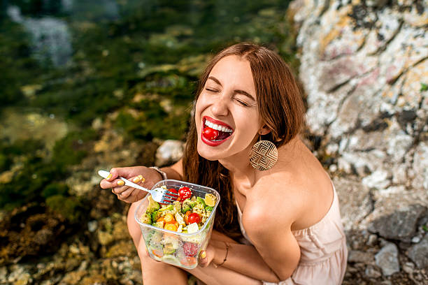femme manger salade diététique à proximité de la rivière - young adult beach people cheerful photos et images de collection