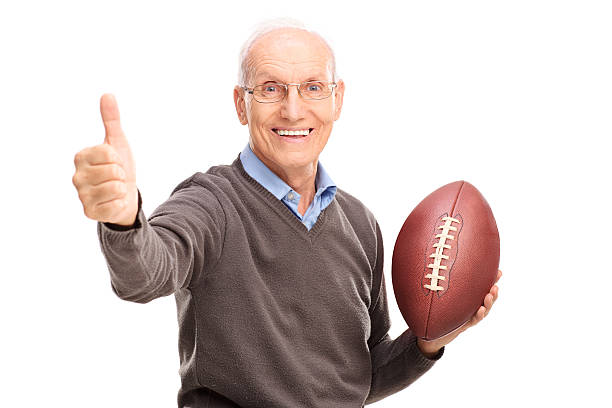 Senior holding a football and giving thumb up Studio shot of a cheerful senior holding an American football and giving a thumb up isolated on white background old football stock pictures, royalty-free photos & images