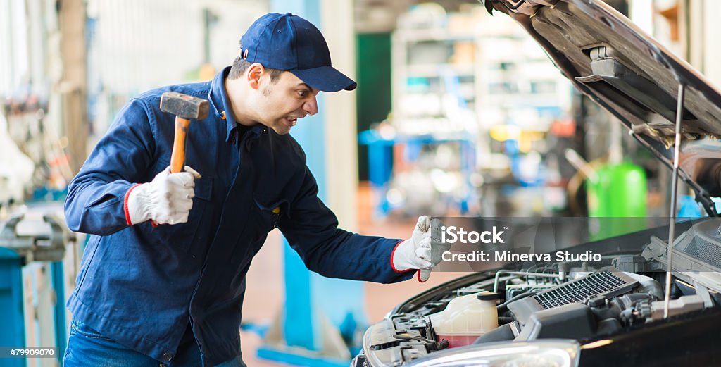 Angry mechanic smashing a car engine Mechanic Stock Photo