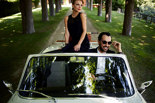 Young rich couple travel on the new white convertible Happy couple enjoying a ride on their luxury convertible in the summer,gorgeous rich woman feels so glad while they riding on cabriolet with sure handsome brunette man, romantic couple at journey trip exclusive travel stock pictures, royalty-free photos & images