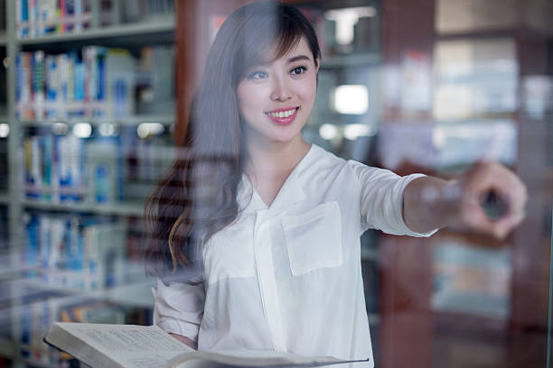 istock Asian beautiful female student touch glass screen in library 479910204