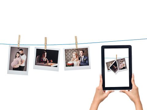 Instant photo prints hanged on string and digital tablet on white background.The photo prints are hanged on string and digital tablet is in human hand.The photos are of wedding, couple,pregnant woman and baby boy.The same photographs are seen on tablet pc screen.The photo was shot with a medium format camera Hasselblad H4D in studio