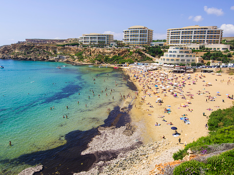 Top view of Golden bay beach with lot of people on sand or in water. In background are some snack bars and hotel capacity. It is located in the northwestern part of Malta near town of Mellieha and is one of nicest beaches on Malta.