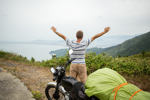 Young man traveling with his motorbike on the Hai Van pass in Vietnam. Arms outstretched for freedom and success.