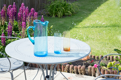 Small round picnic table with a jug of water and glass in a garden on a sunny day