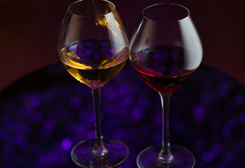 Two glases with wine, dark background, puple defocused lights reflection