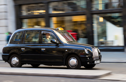 London, UK - 16th March 2014: A Taxi moving down a street in London with shop windows in the background
