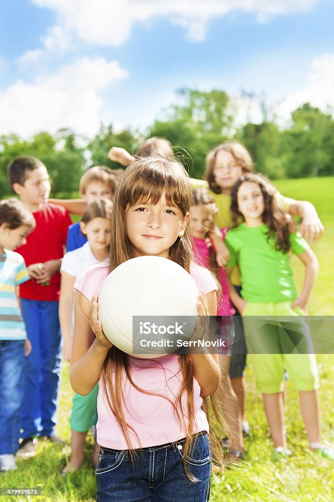 Girl with ball and her team Nice little girl with the ball standing in the park with her team behind her Child Stock Photo