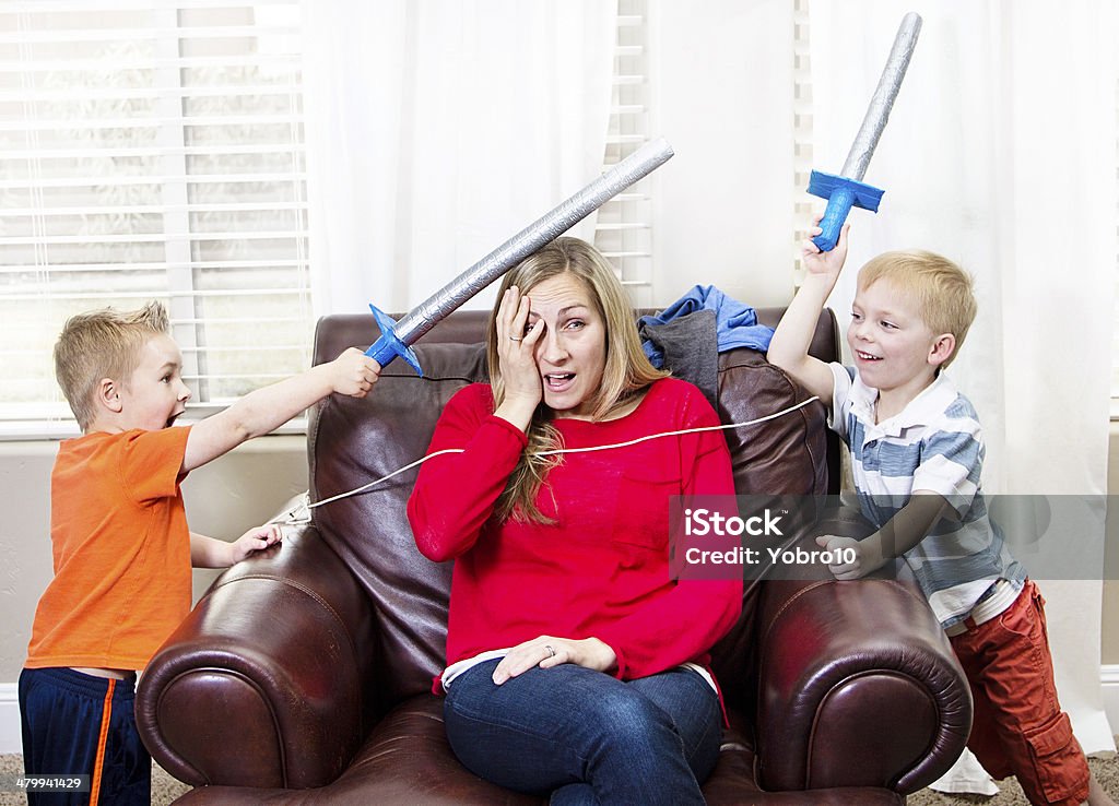 Young Mother overwhelmed by her kids Young Mother overwhelmed with home life as two little boys have a sword fight around her Mother Stock Photo