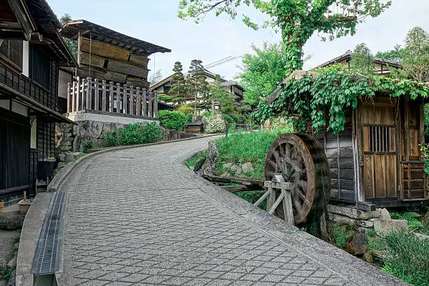 A view of Tsumago, a traditional Japanese post town. Nagiso, Kiso District. Traditional buildings with a motion blurred waterwheel, nobody, street view, horizontal composition. 