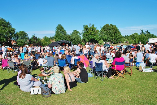 Tenterden, England - July 4, 2015: The audience sit on the grass in the local park at the annual free Tentertainment music festival. The community event was first held in 2008.