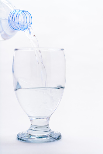 A glss of water being poured out of a bottle on a white background.