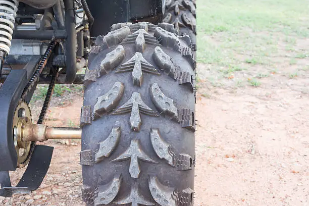 wheel of Dirty ATV stands on the ground in rubber tree field 