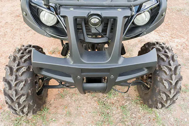 front wheel of Dirty ATV stands on the ground in rubber tree field