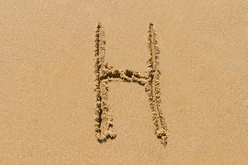 Letter H of the alphabet written on sand with upper case.