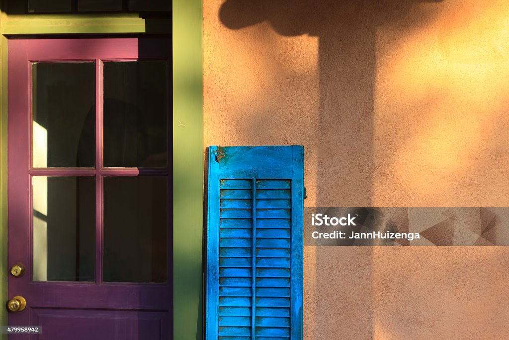 Santa Fe Style: Porch with Colorful Door, Shutter, Adobe Wall Santa Fe Style: a colorful porch with a purple and green door, blue shutter, orange adobe wall with sunlight and shadows. Shot in Santa Fe, New Mexico. Copy space on the yellow wall. Adobe - Material Stock Photo
