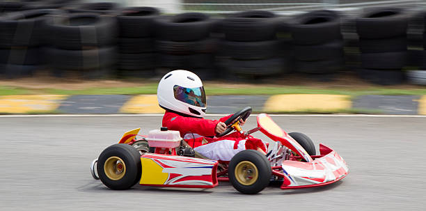 Panning shot of young boy in a gokart Asian boy wearing red and white race suit and white helmet practising in a gokart. Shot with a Canon 1DmkIV with slow shutter speed to create a panning speed blur effect with rubber tires in the background. go carting stock pictures, royalty-free photos & images