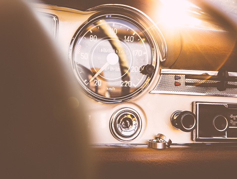 Man's and woman's wedding rings resting on the retro styled dashboard of a classic vintage car with afternoon sun flare