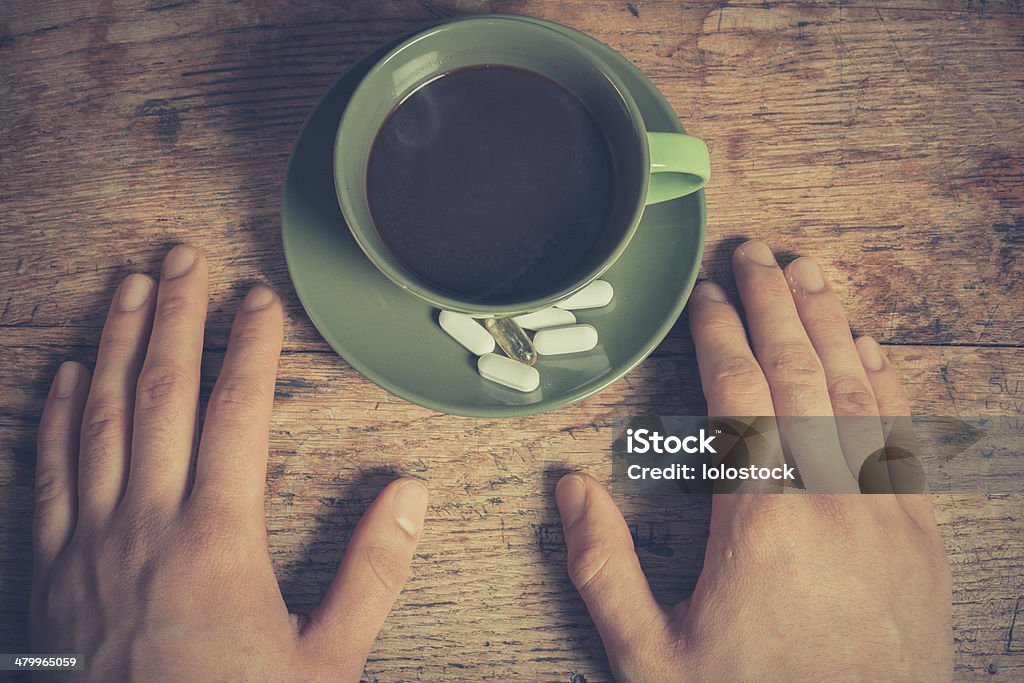 Man having pills and coffee A man is resting his hands on a table with a cup of coffee and some pills Acetylsalicylic Acid Stock Photo