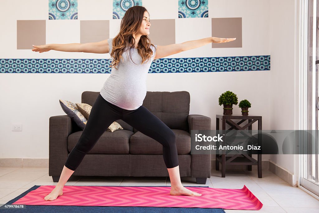 Warrior yoga pose and pregnant Pretty young brunette doing some yoga exercises at home during her pregnancy 20-29 Years Stock Photo